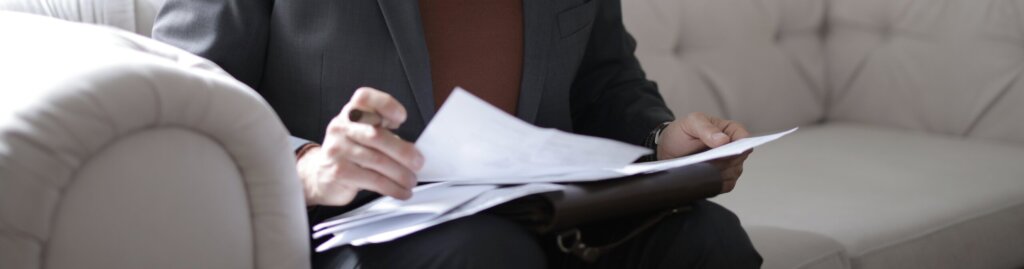 person sits on a couch while holding a paper contract and pen