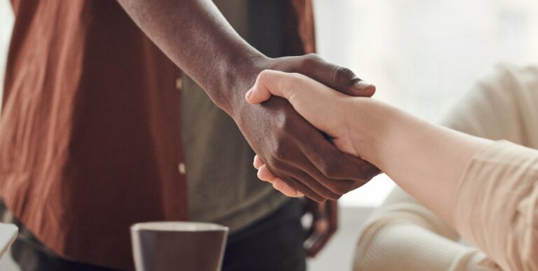 two people shake hands across a conference table where one person is standing and one person is seated
