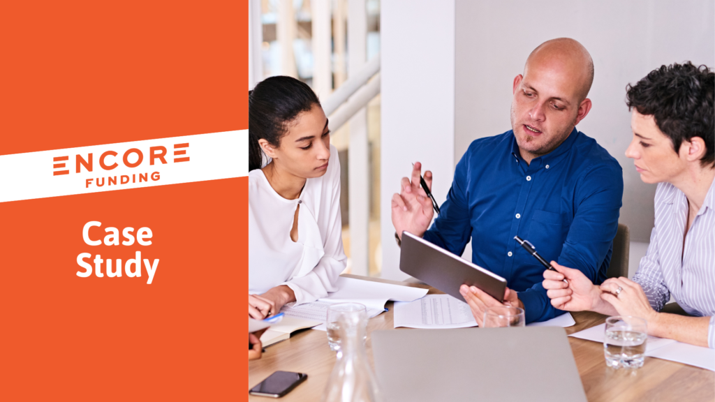 Three people sit at a table and review payroll funding materials on a tablet