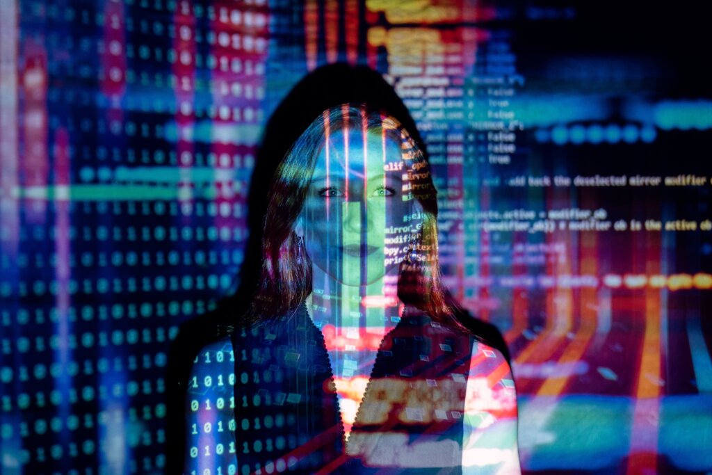 AI tech tools for staffing make it easy for staffing agencies to save time and money. This photo is of a person in a dark room with colorful lines of code being projected over their face and upper body.