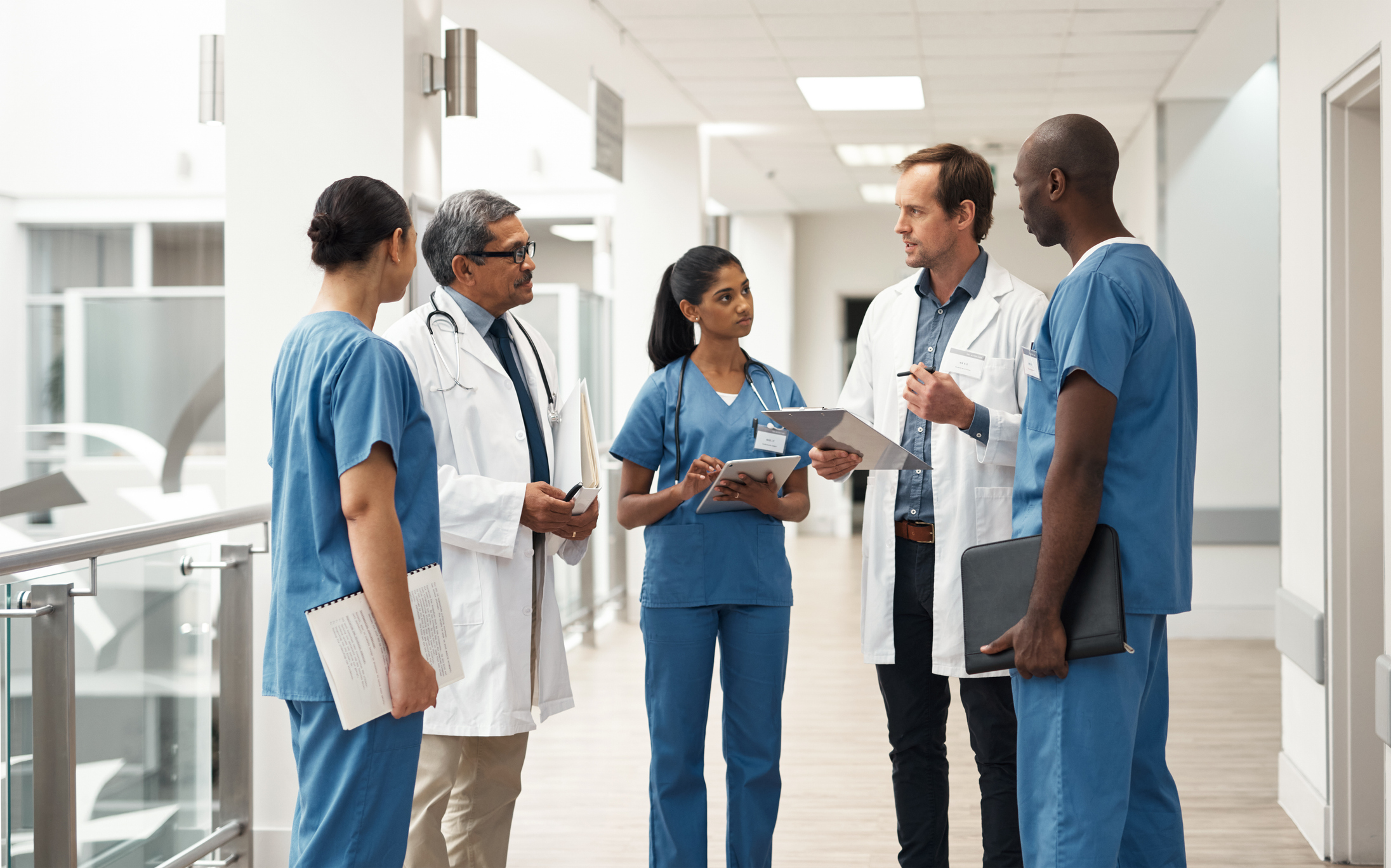 A group of doctors and nurses stand near each other in a healthcare facility. They are in a friendly but serious conversation.