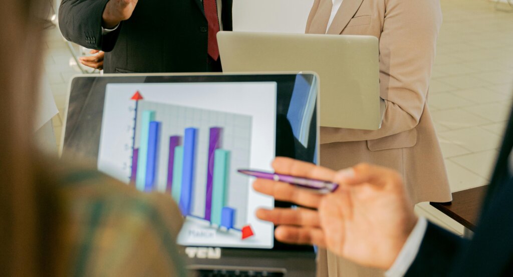 Two coworkers face a laptop to view a blue and purple bar chart that shows business growth.
